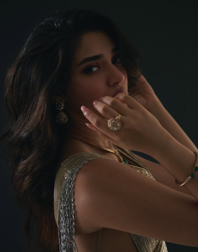 Krithi Shetty wearing an elegant golden gown, posing gracefully in a studio photoshoot with a dark background, showcasing a stylish and glamorous look.