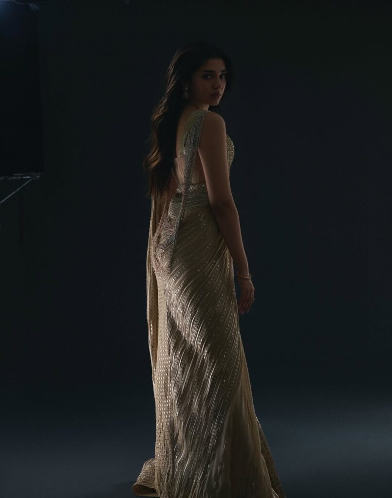 Krithi Shetty wearing an elegant golden gown, posing gracefully in a studio photoshoot with a dark background, showcasing a stylish and glamorous look.