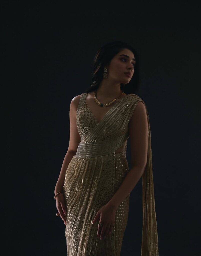 Krithi Shetty wearing an elegant golden gown, posing gracefully in a studio photoshoot with a dark background, showcasing a stylish and glamorous look.