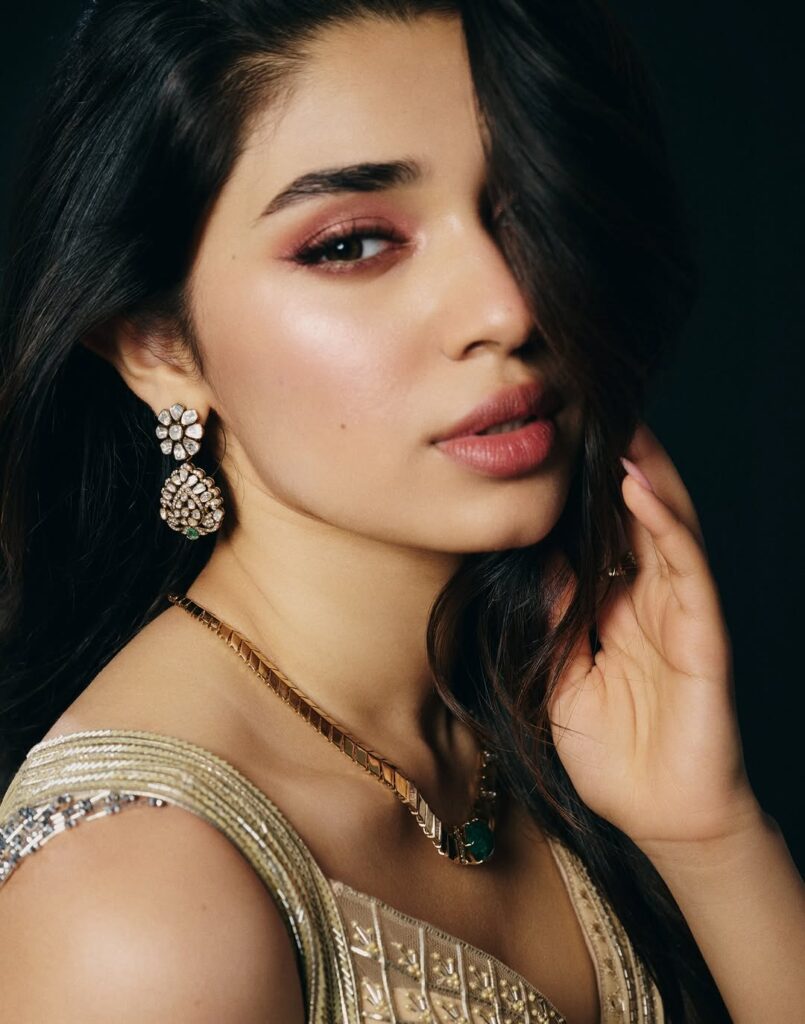Krithi Shetty wearing an elegant golden gown, posing gracefully in a studio photoshoot with a dark background, showcasing a stylish and glamorous look.