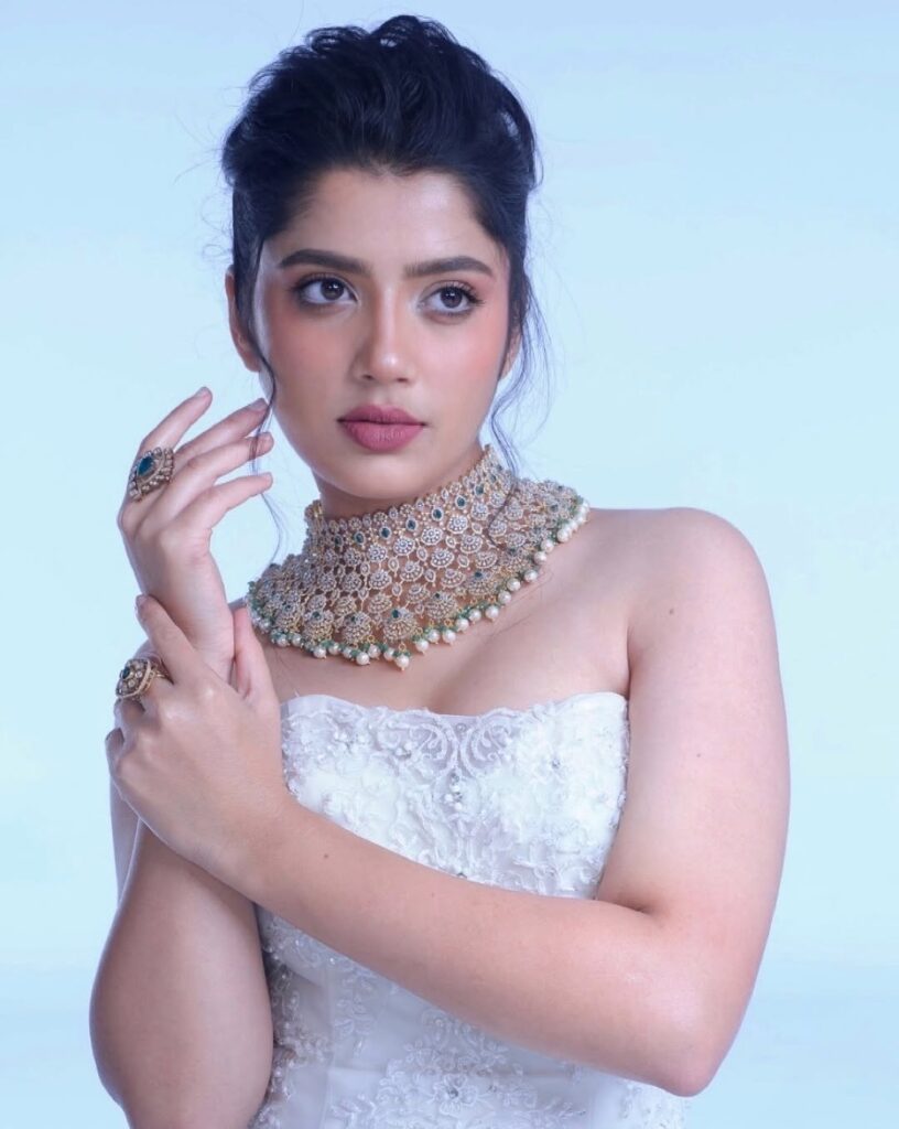 Devika Bhatt in an elegant white strapless dress with stunning traditional gold necklace and blue stone jewellery, posing gracefully for a photoshoot - Kannada actress